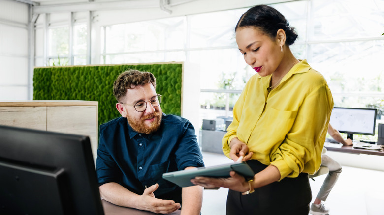 An office manager showing some documents on a digital tablet to her colleague in a bright, modern office space.