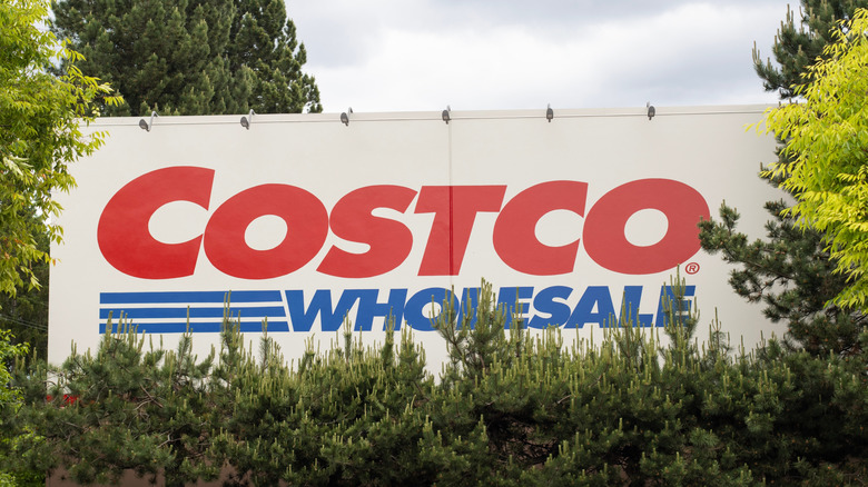 A Costco sign obstructed by trees.