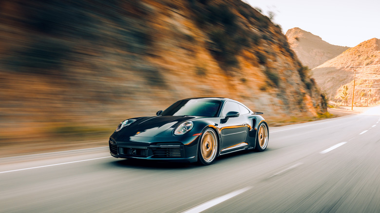 A 992 Porsche 911 Turbo on a canyon road, front 3/4 view, aftermarket wheels