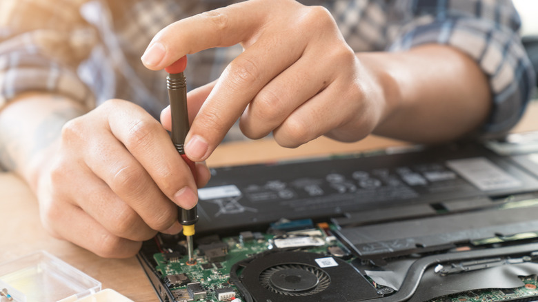person unscrewing the internals of a laptop