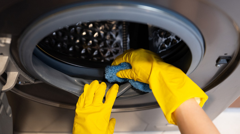 A person wearing rubber gloves cleaning a washing machine.