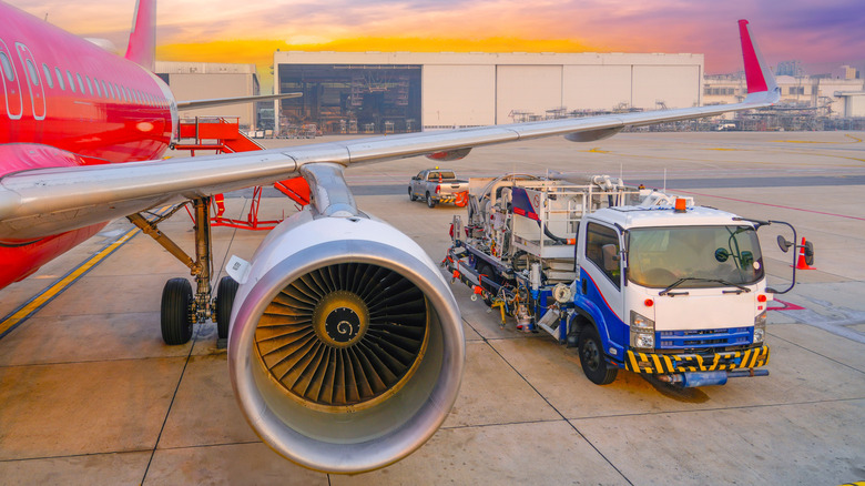An aircraft prepares to be fueled by a truck on the runway at sunset