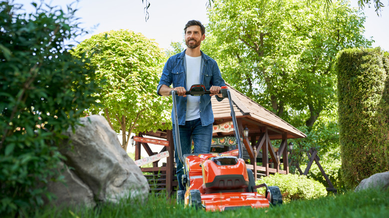Smiling bearded man cutting grass with orange electric mower