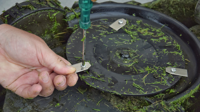 man changing lawnmower blade with wet grass visible
