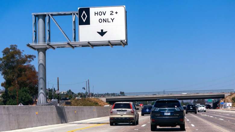 HOV sign board saying 2+ only, a gold Honda CR-V driving on it