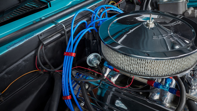 A muscle car engine bay with exposed spark plug wires.