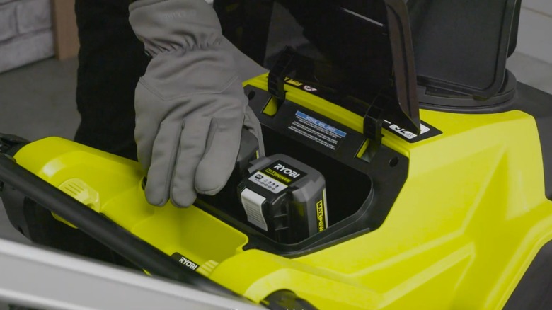 A person putting Ryobi batteries into a snowblower.
