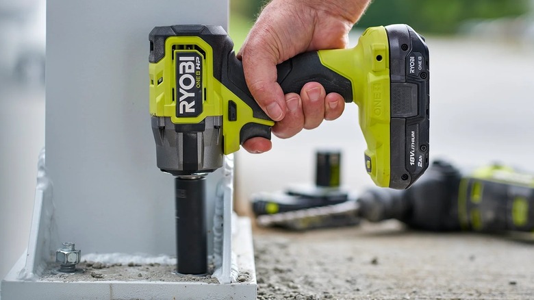 Hand holding Ryobi impact wrench with other Ryobi tools and batteries in the background