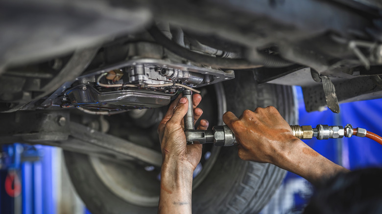 Mechanic servicing transmission with fill hose