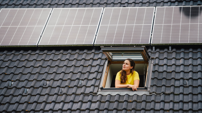 Woman looking out window with solar panel installed on roof