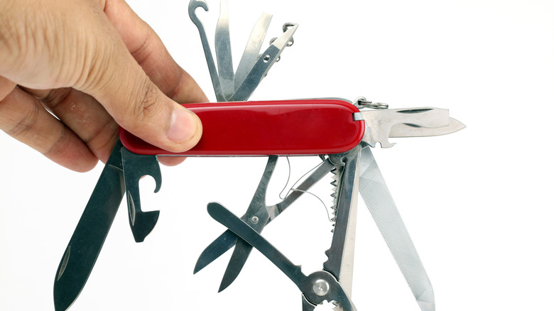 A standard multi-tooled Swiss army knife, being held by the left hand of someone who is not otherwise visible. All the tools in the swiss army knife are open.