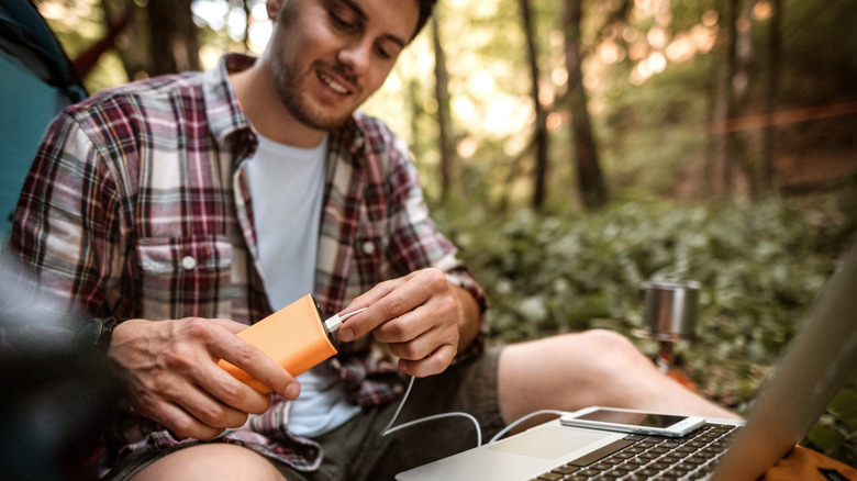 Young casually clothed camper working from his camp, connecting power bank to his laptop