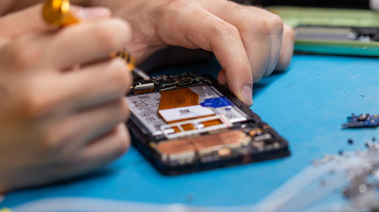 Someone repairing a smartphone on a table top with visible interiors