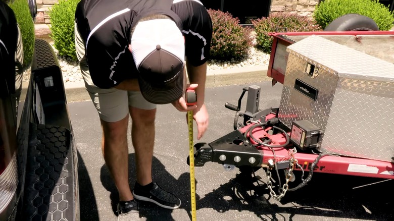 A Man Using A Measuring Tape To Determine The Distance Between A Trailer Coupler And The Ground