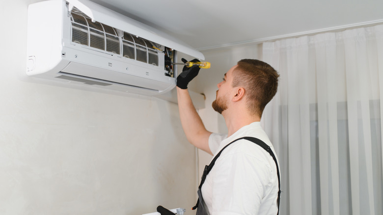A person repairing a wall-mounted air conditioner unit.
