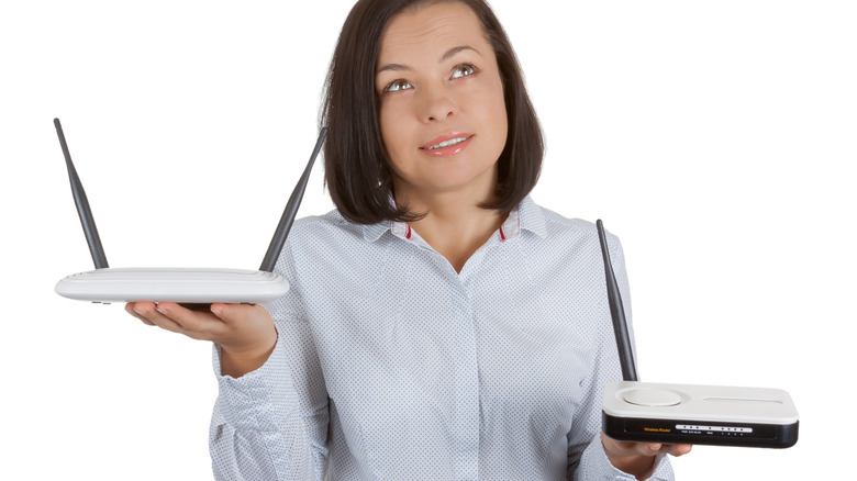 A woman with dark hair and a white shirt holding two wireless modem routers, one in each hand, on a white background