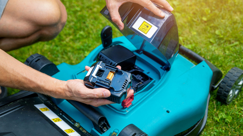 A person putting the battery into an electric lawn mower.