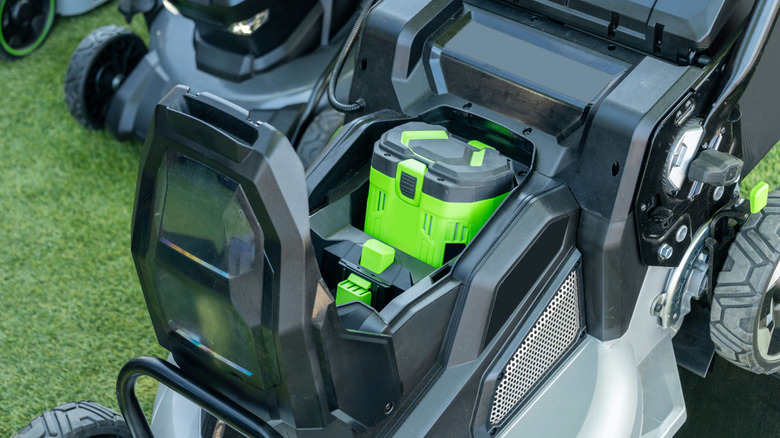 An electric lawn mower with an opened battery compartment.