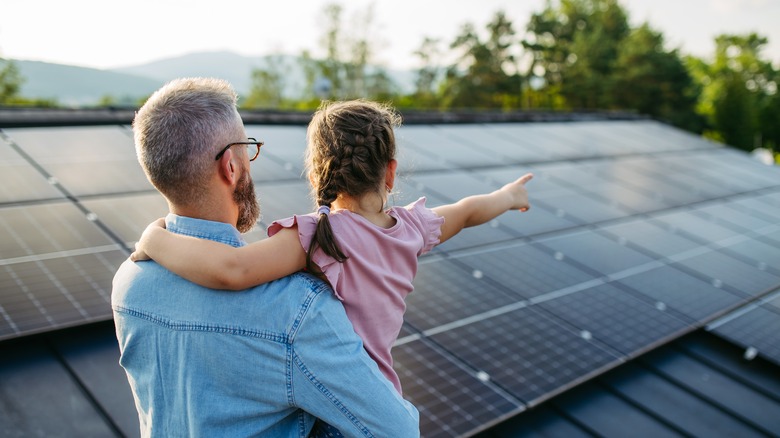 Rear view of dad with girl on roof with solar panels