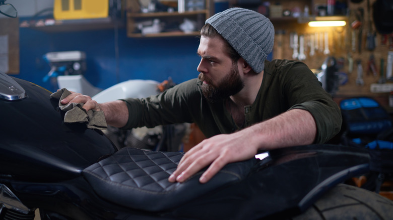 A motorcycle rider cleaning the bike's fewl tank with a cloth in his garage