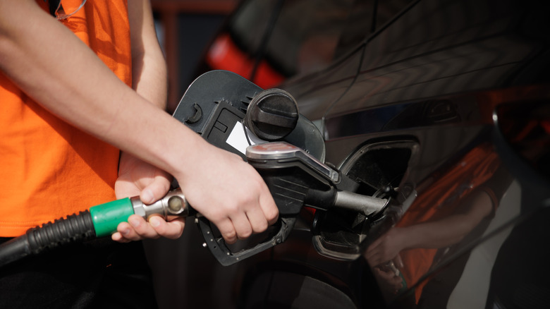 A person holding a gas pump while filling up a car with fuel