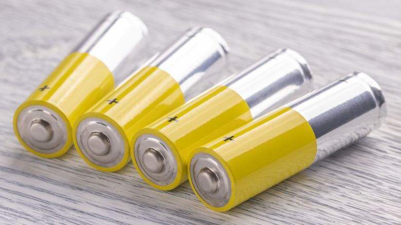 A close-up of four AA batteries lying on a white/gray wooden table.