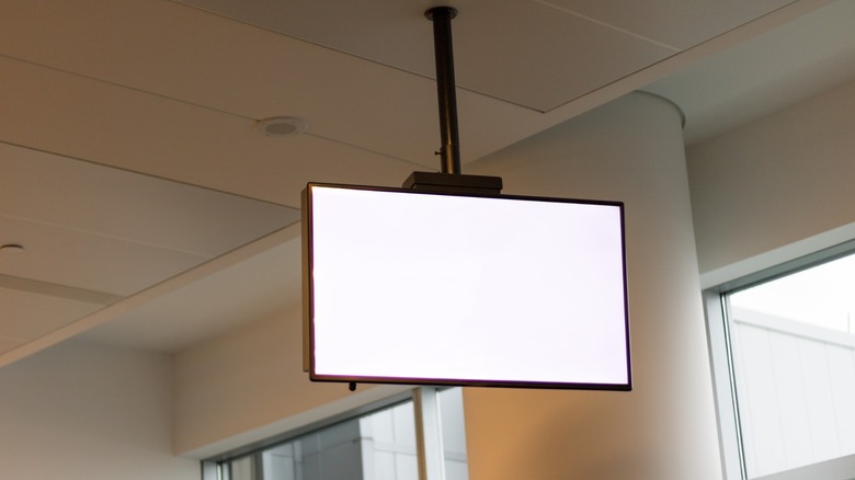 A television suspended from a ceiling by a single pole mount.