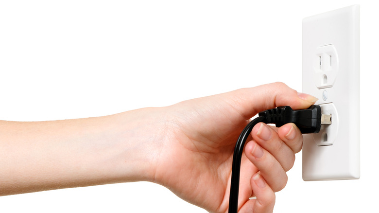 Person plugging two-prong plug into three-prong outlet
