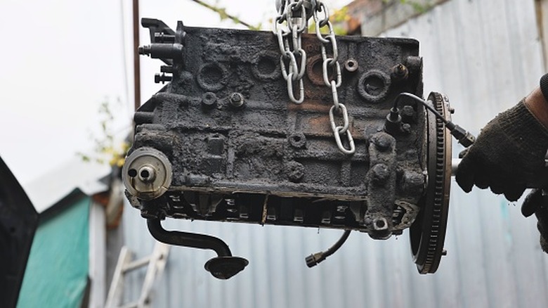 An engine block full of carbon build-up being hoisted out of a car with an engine hoist