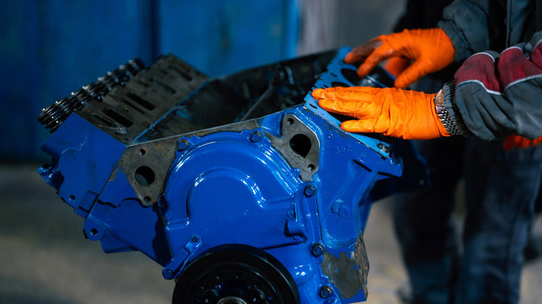A gloved mechanic handling a blue engine block