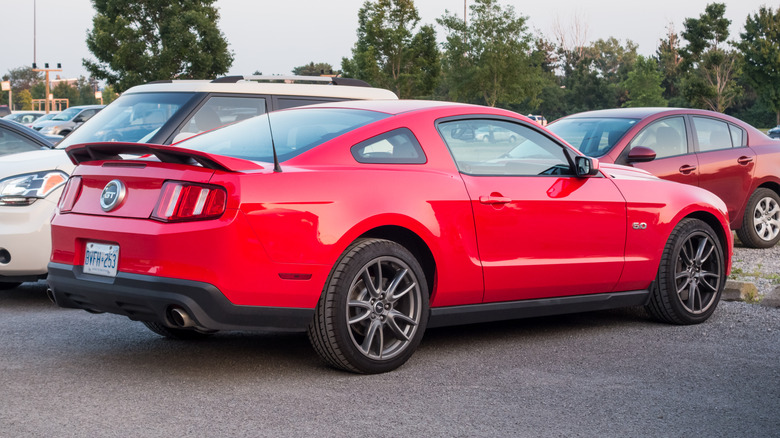 A 2011 Ford Mustang GT in red on a parking lot, rear 3/4 view