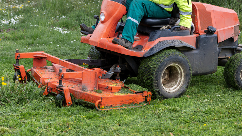 A commercial mower deck cuts along the edge of grass and weeds