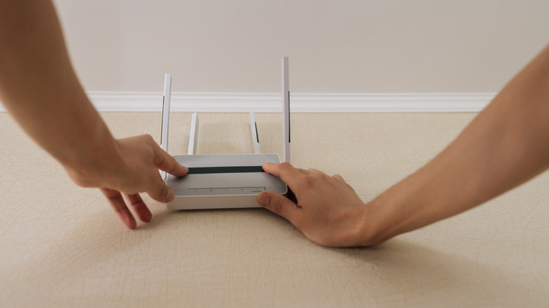 A close-up of persons hand placing a white/gray Wi-Fi router on the floor