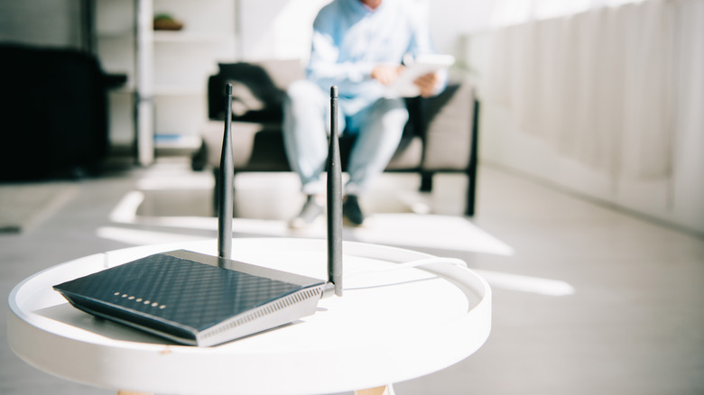 A zoomed focus on a black Wi-Fi router placed on a small round white table, with a person sitting in the distance