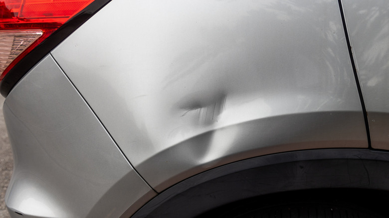 Minor scratches and a dent in the body of a silver car