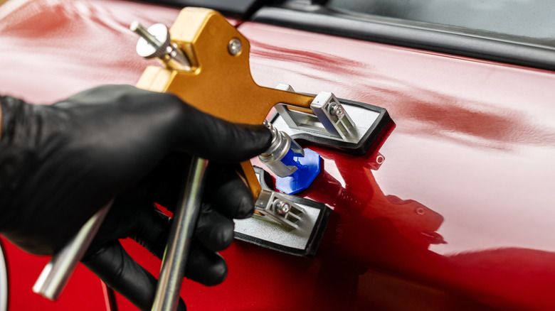 Hand using a dent puller to fix a dent in a red car door