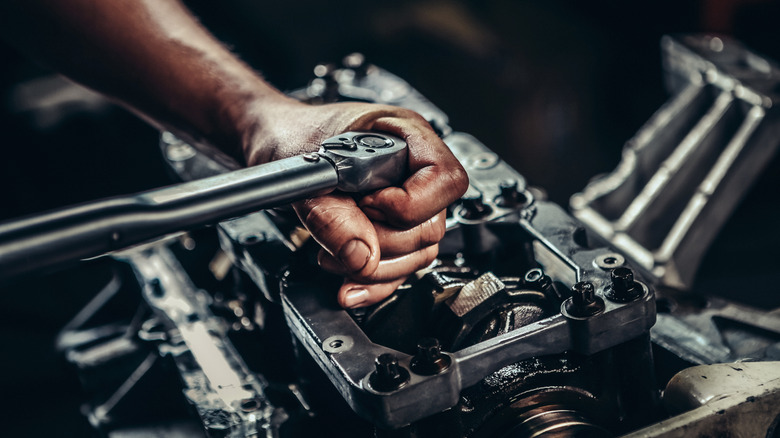 Mechanic servicing bottom-end of V8 engine with torque wrench