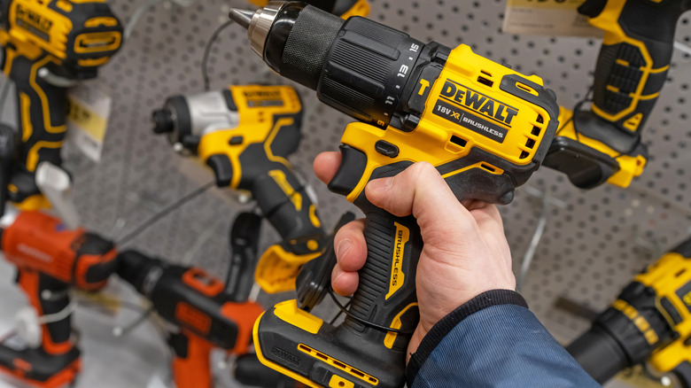 A person holding a DeWalt cordless power drill, with other DeWalt products on display in the background
