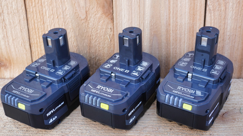 Three Ryobi power tool batteries lined up on wood surface