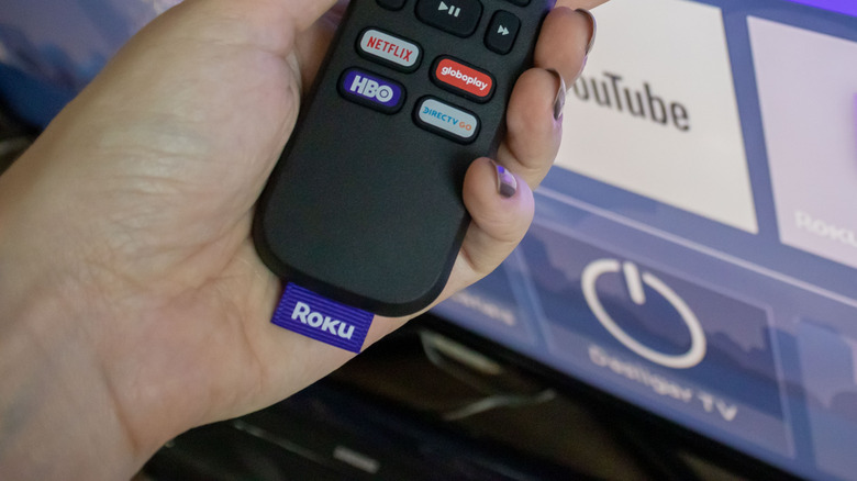 person holding a Roku remote in front of a TV