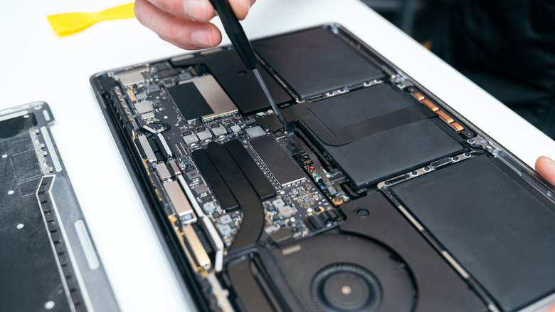 Hand holding screwdriver pointing to internal laptop battery
