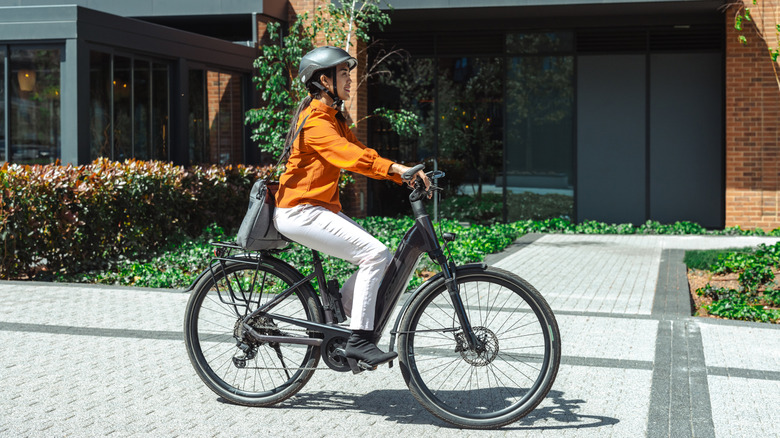 Woman riding an E-bike on the sidewalk of a city.