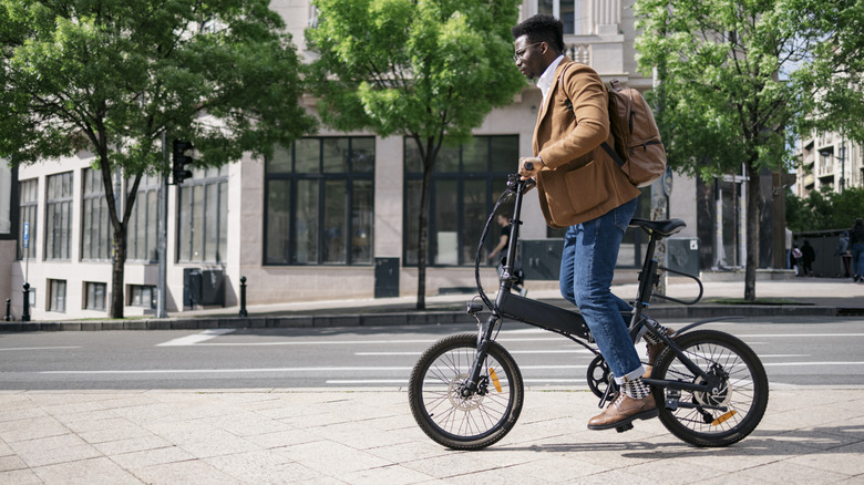 A young man casually riding his electric bicycle to work through the city on a sidewalk.