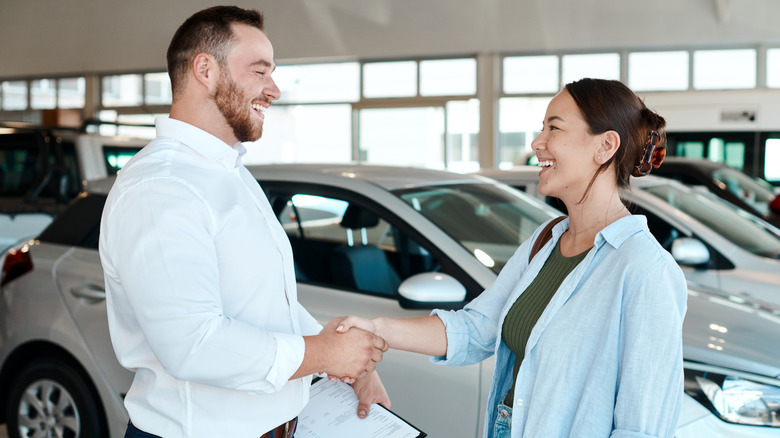 A man and woman shaking hands in a car dealership showroom