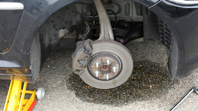 Car disc brake with puddle on ground, indicating brake fluid leak