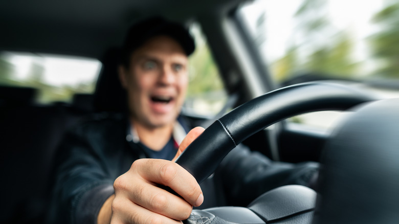 Driver panicking while gripping steering wheel, view from behind instrument cluster, blurred background with focus on wheel