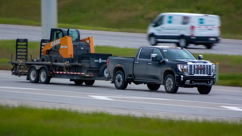 A GMC Sierra towing a trailer with a construction vehicle on it, front 3/4 view