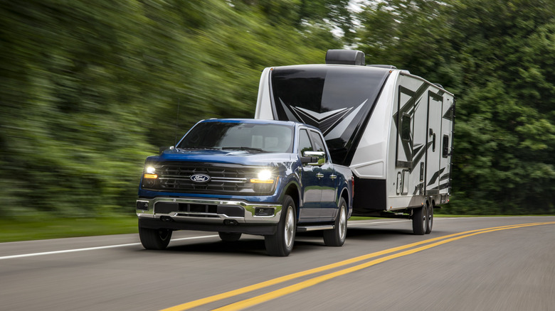 A 2024 Ford F-150 in blue towing a camping trailer, front 3/4 view
