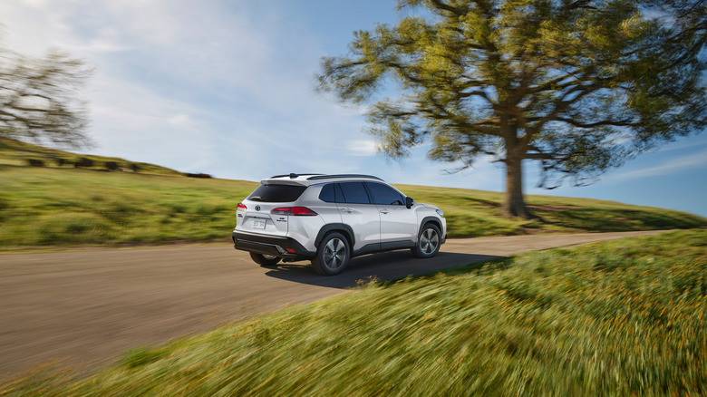 Rear 3/4 view of a white Toyota Corolla Cross driving over a hill