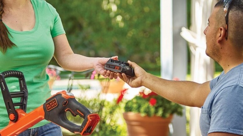 Man handing over Black and Decker battery to woman with power tool